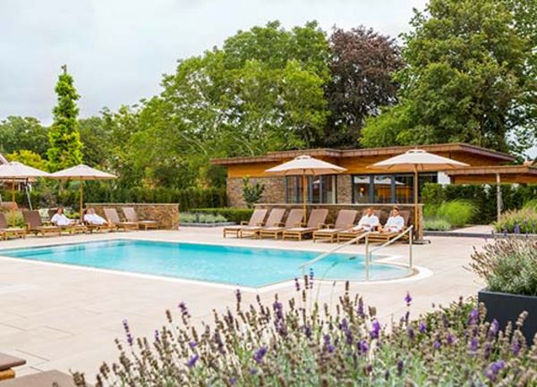 Ansicht eines Hotelpools draußen mit Sonnenschirmen im Grünen