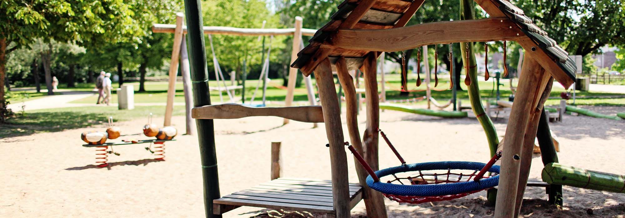 Ein kleines Haus, eine Nestschaukel und andere Spielgeräte auf einem Spielplatz