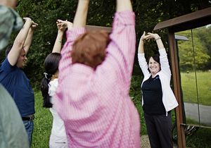 Eine kleine Menschengruppe macht einer Frau Fitnessübungen nach